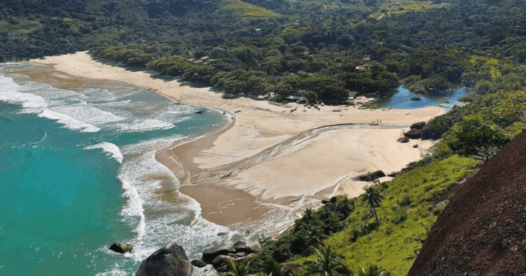 Vista aérea da Praia do Bonete, em Ilhabela, mostrando o mar azul-esverdeado com ondas suaves, a larga faixa de areia clara, o encontro do rio com o mar e a densa vegetação preservada ao redor, destacando um dos cenários mais selvagens e paradisíacos do litoral norte de São Paulo.