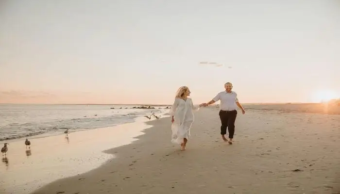 Casal caminhando na praia ao pôr do sol sorrindo, exemplo que morar na praia faz bem para saúde
