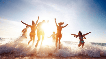 Grupo de pessoas se divertindo na beira do mar durante o pôr do sol, pulando e brincando entre as ondas em um clima de férias relaxantes no litoral