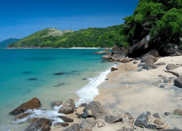 Paisagem de uma das Melhores praias do litoral norte de São Paulo com mar azul, areia clara, pedras naturais e mata preservada ao fundo, representando a beleza e tranquilidade da região.