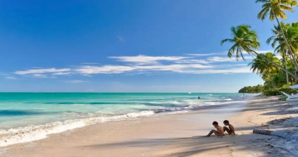 Praia de Antunes em Maragogi com duas crianças na areia e coqueiros com o mar de aguas verdes e ceu azul