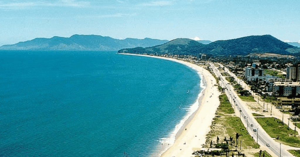 Imagem aérea Praia Martim de Sá (Caraguatatuba), mar calmo, longa faixa de areia com a estrada passando ao lado no litoral norte de SP