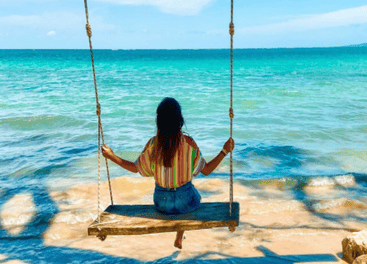 Menina na gangorra na praia em Moitas (CE) com mar de aguas cristalinas