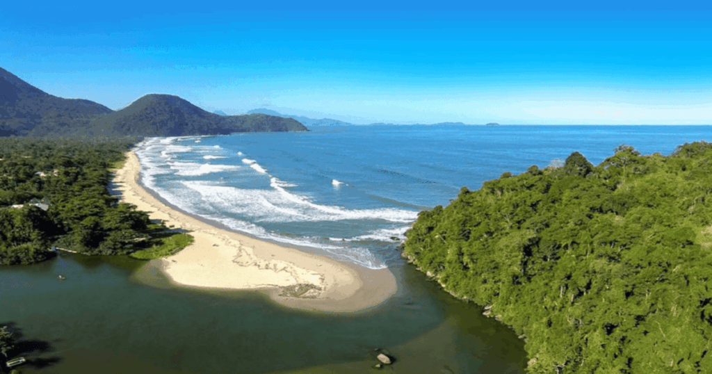 Vista aérea da Praia de Itamambuca, em Ubatuba, mostrando o mar azul com ondas perfeitas para surf, a longa faixa de areia clara, o encontro do rio com o oceano e a densa vegetação preservada ao redor, destacando um dos cenários mais naturais e exuberantes do litoral norte de São Paulo.