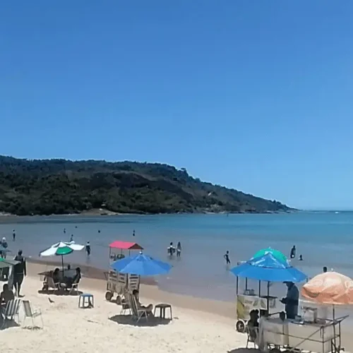 Foto do canto esquerdo da praia do morro, em um dia de semana ensolarado, com banhistas na areia e vendedores, exemplo de uma das praias mais baratas do Espírito Santo