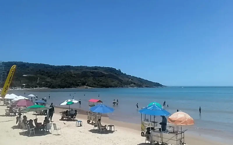 Foto do canto esquerdo da praia do morro, em um dia de semana ensolarado, com banhistas na areia e vendedores, exemplo de uma das praias mais baratas do Espírito Santo