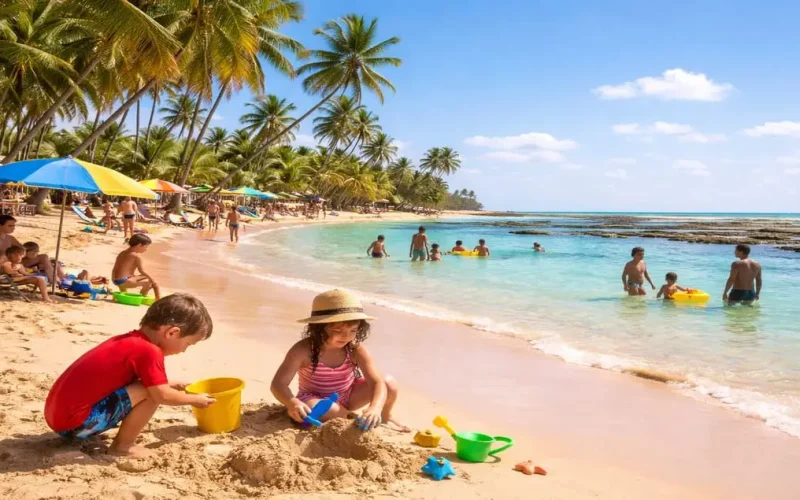 Crianças brincando na areia e no mar calmo em uma das melhores praias para crianças na Bahia, com águas rasas, palmeiras e famílias aproveitando o dia.