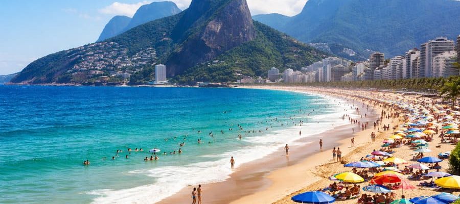Vista de praia do Rio de Janeiro com mar azul e faixa de areia cheia de banhistas, destino ideal para quem busca praia barata e passagem para o Rio de Janeiro.