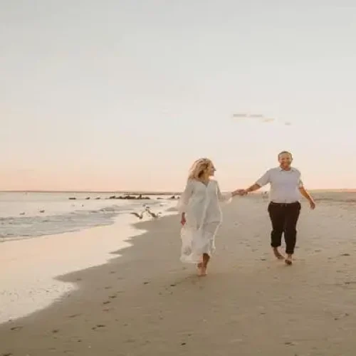 Casal caminhando na praia ao pôr do sol sorrindo, exemplo que morar na praia faz bem para saúde
