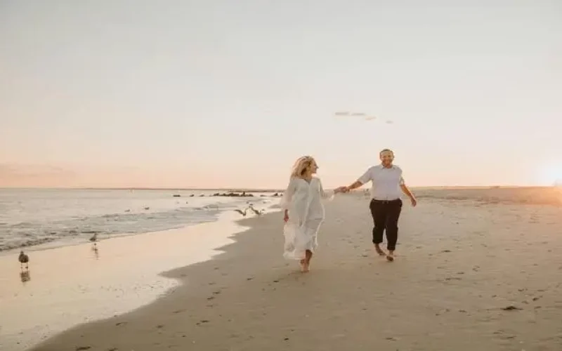 Casal caminhando na praia ao pôr do sol sorrindo, exemplo que morar na praia faz bem para saúde