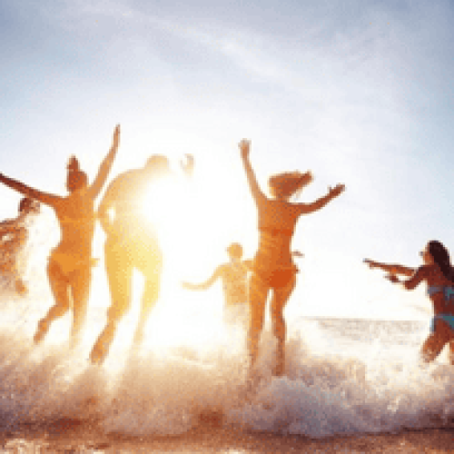 Grupo de pessoas se divertindo na beira do mar durante o pôr do sol, pulando e brincando entre as ondas em um clima de férias relaxantes no litoral