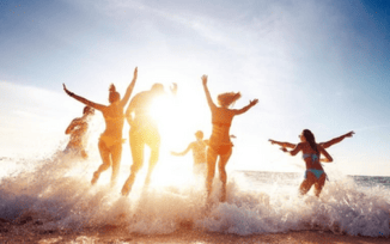 Grupo de pessoas se divertindo na beira do mar durante o pôr do sol, pulando e brincando entre as ondas em um clima de férias relaxantes no litoral