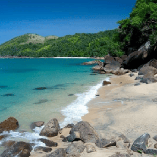 Paisagem de uma das Melhores praias do litoral norte de São Paulo com mar azul, areia clara, pedras naturais e mata preservada ao fundo, representando a beleza e tranquilidade da região.
