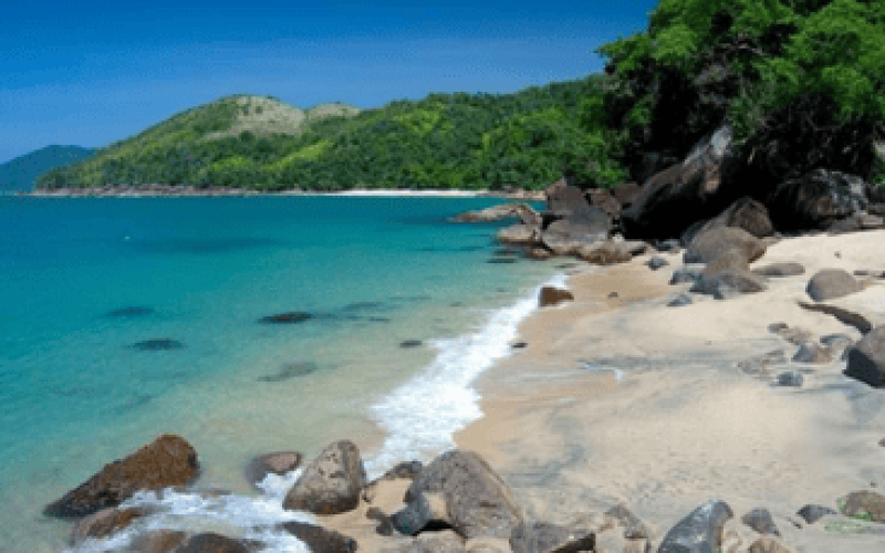 Paisagem de uma das Melhores praias do litoral norte de São Paulo com mar azul, areia clara, pedras naturais e mata preservada ao fundo, representando a beleza e tranquilidade da região.