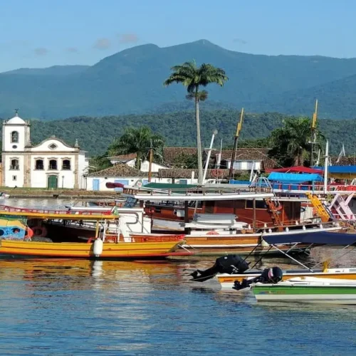 Vista do porto de Paraty com embarcações coloridas e o cenário deslumbrante das montanhas, refletindo a história, cultura e natureza exuberante dessa cidade histórica e charmosa no litoral fluminense.