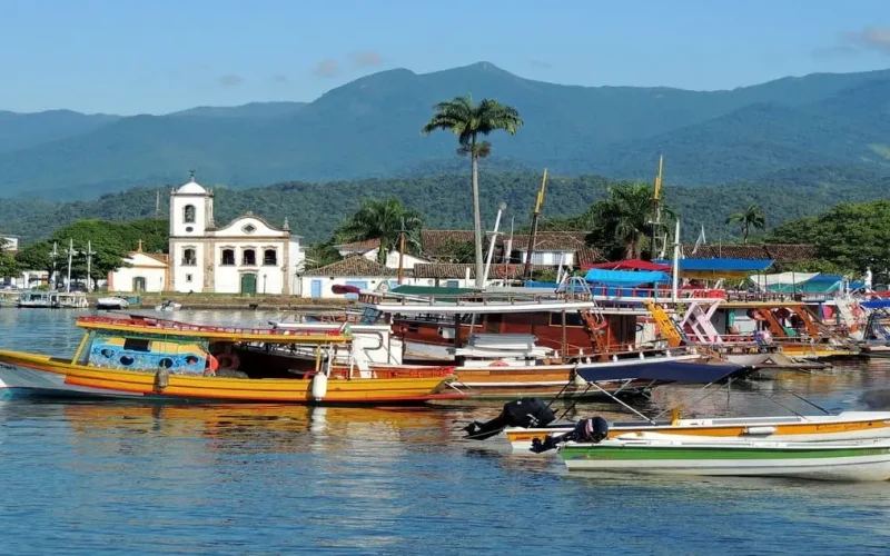 Vista do porto de Paraty com embarcações coloridas e o cenário deslumbrante das montanhas, refletindo a história, cultura e natureza exuberante dessa cidade histórica e charmosa no litoral fluminense.